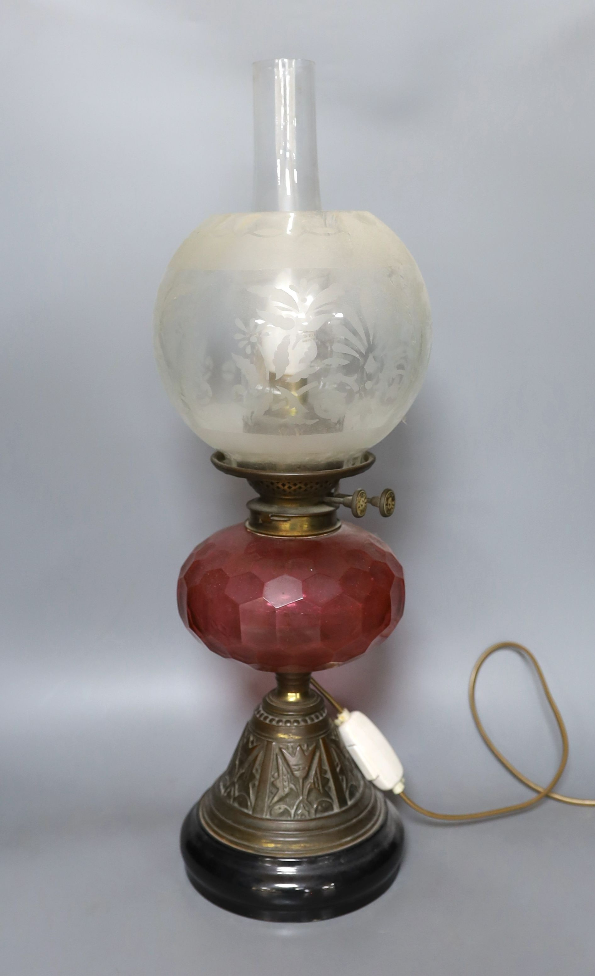 An Edwardian oil lamp with ruby glass font, later inverted to electricity, 57 cms high including funnel.